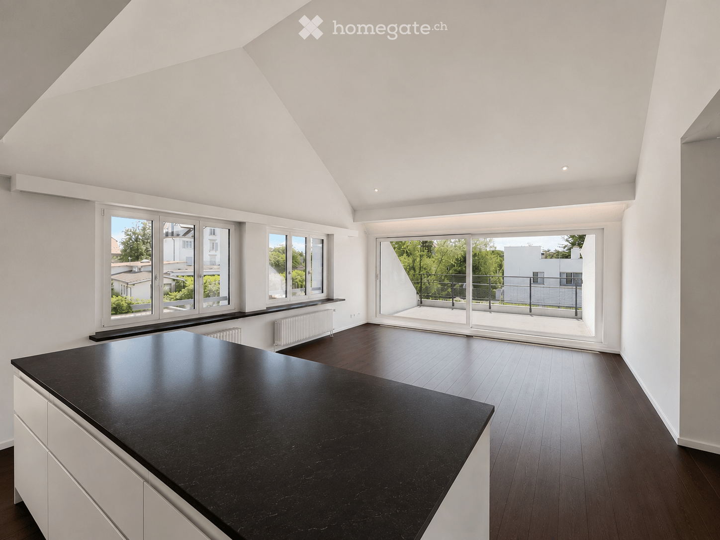 Modern kitchen with a black countertop, white cabinets, and large windows offering a view of the balcony and greenery outside.