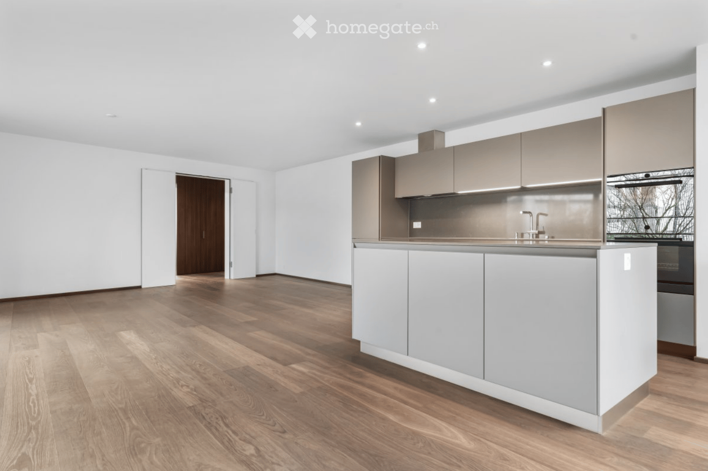 Modern kitchen with light grey cabinets, a central island, and a sleek faucet, featuring a wooden floor and white walls.