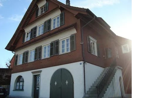 Two-story traditional house with red brick facade, white trim, multiple windows with shutters, and a green garage door.