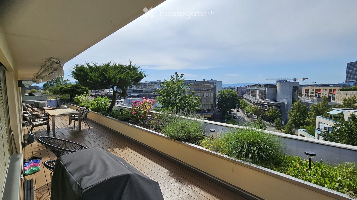 Balcony with wooden decking, outdoor furniture, plants, and a city view.