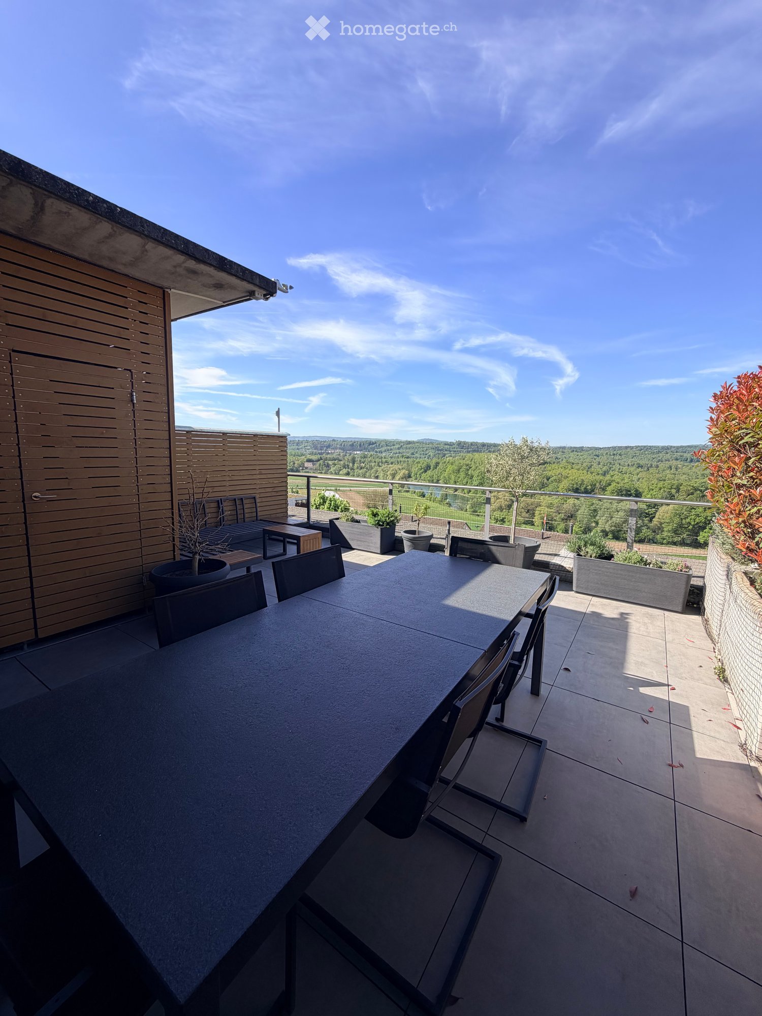 Modern rooftop terrace with a dining table, chairs, and a scenic view of the countryside.