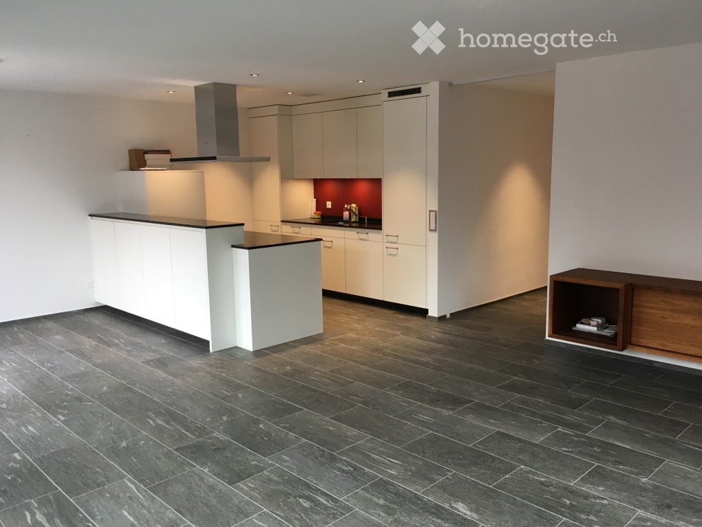 Modern kitchen with white cabinets, a central island, dark tiled floor, and a range hood. A wooden shelf is visible on the right side.