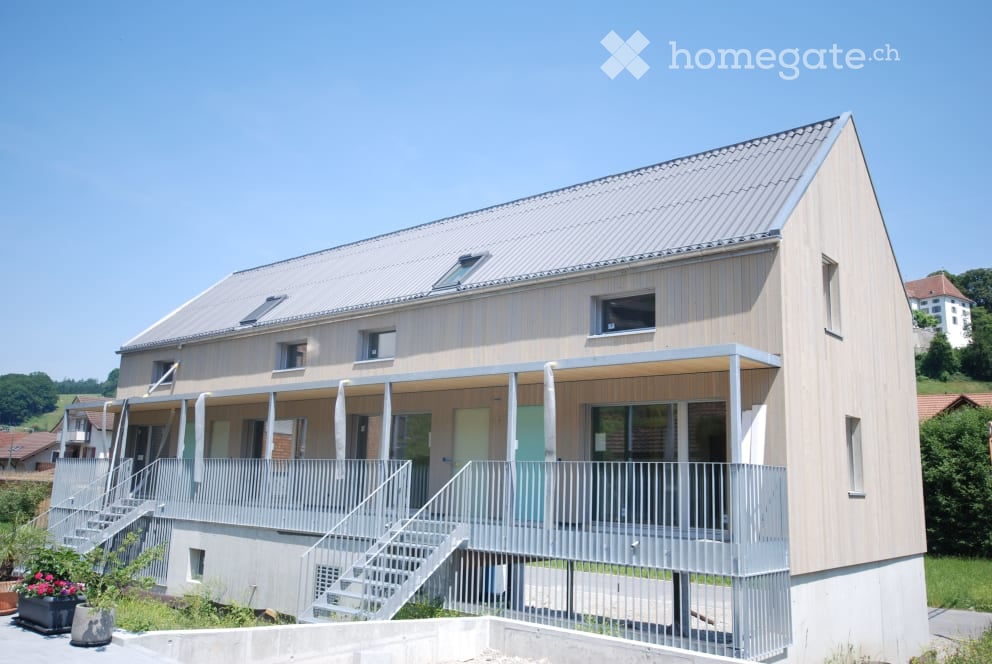 Modern two-story building with a flat roof, large windows, and a covered balcony area on the first floor.