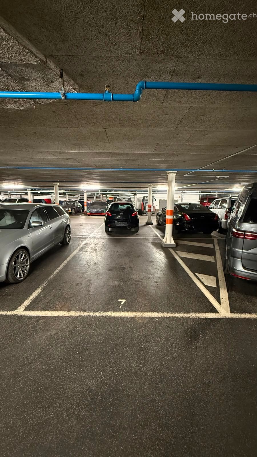 Underground parking lot with several parked cars, marked parking spaces, and concrete pillars for support.