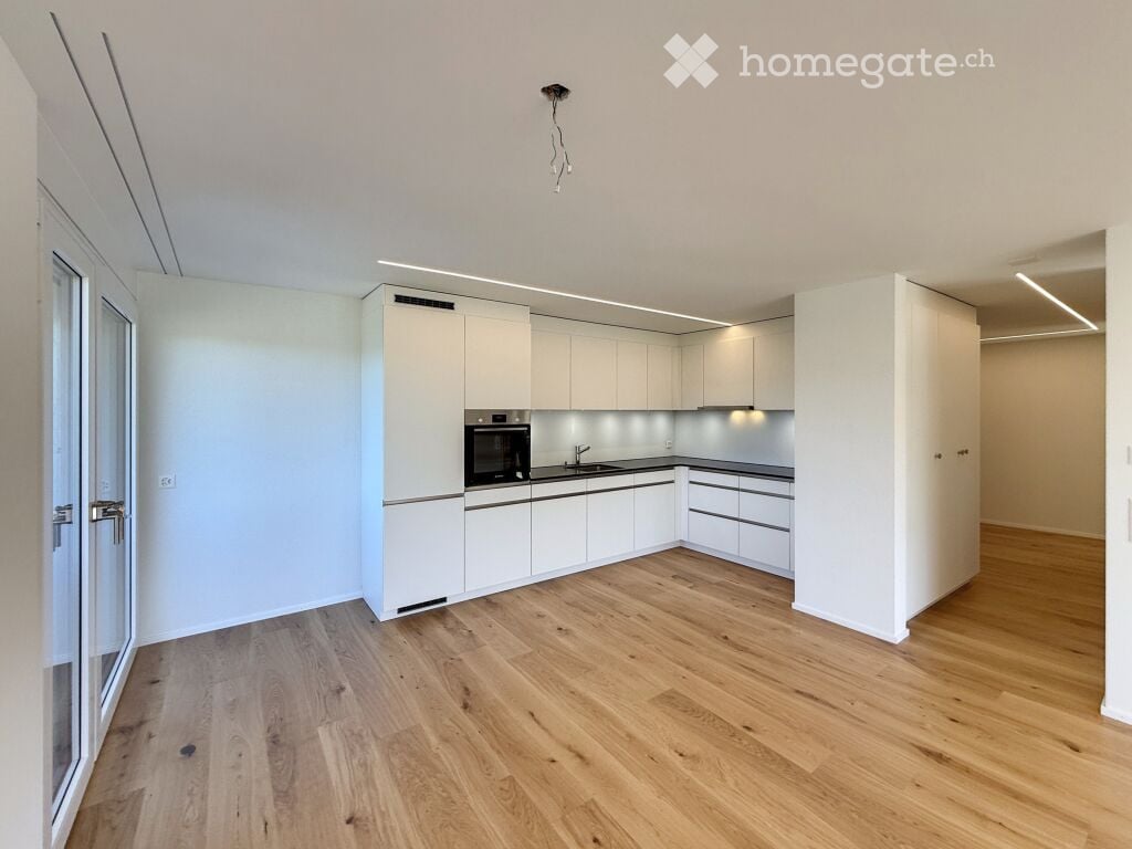 Modern kitchen with white cabinets, wooden flooring, and built-in oven and sink.