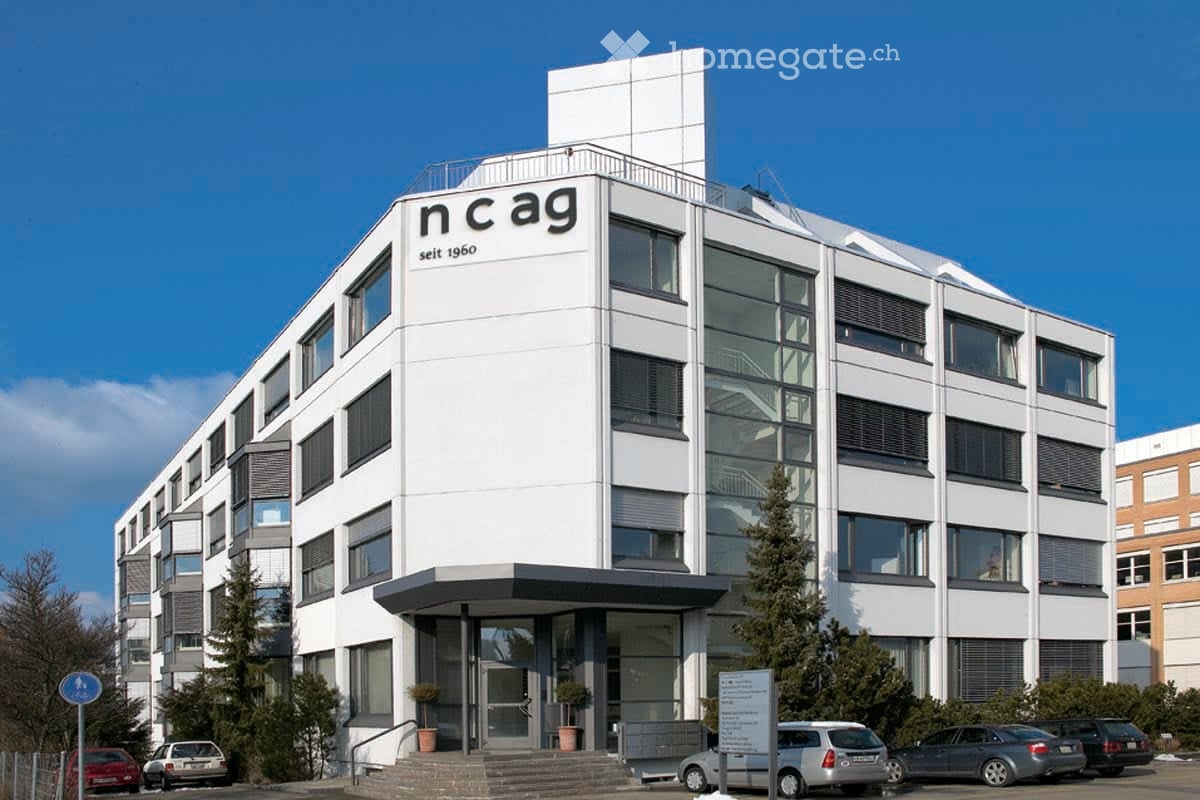 Modern multi-story building with white facade, large windows, and signage reading "ncag seit 1960".