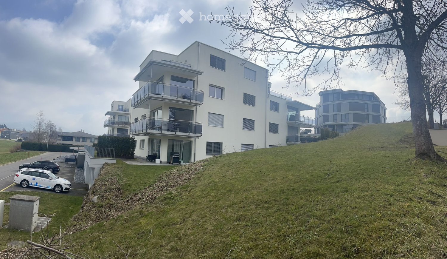White multi-story building with balconies, located on the side of the hill, with a parking area below