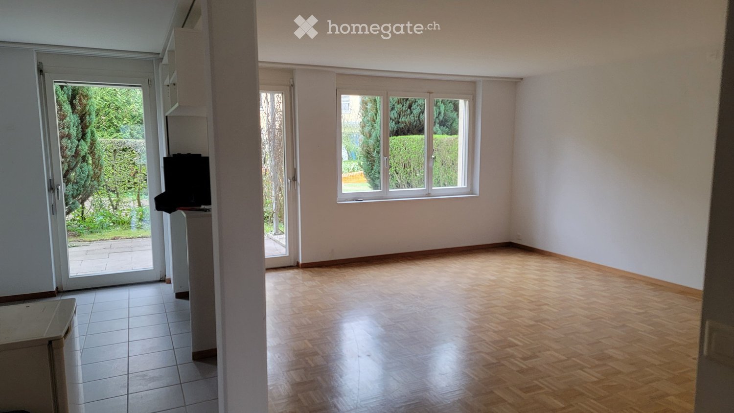 Empty room with wooden flooring, white walls, large windows, and a sliding glass door leading to an outdoor area.