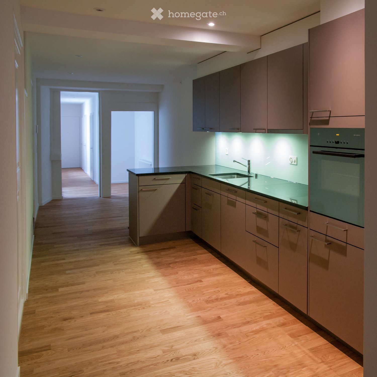 Modern kitchen with light wood flooring, sleek cabinetry, and built-in appliances including a sink, faucet, and oven.