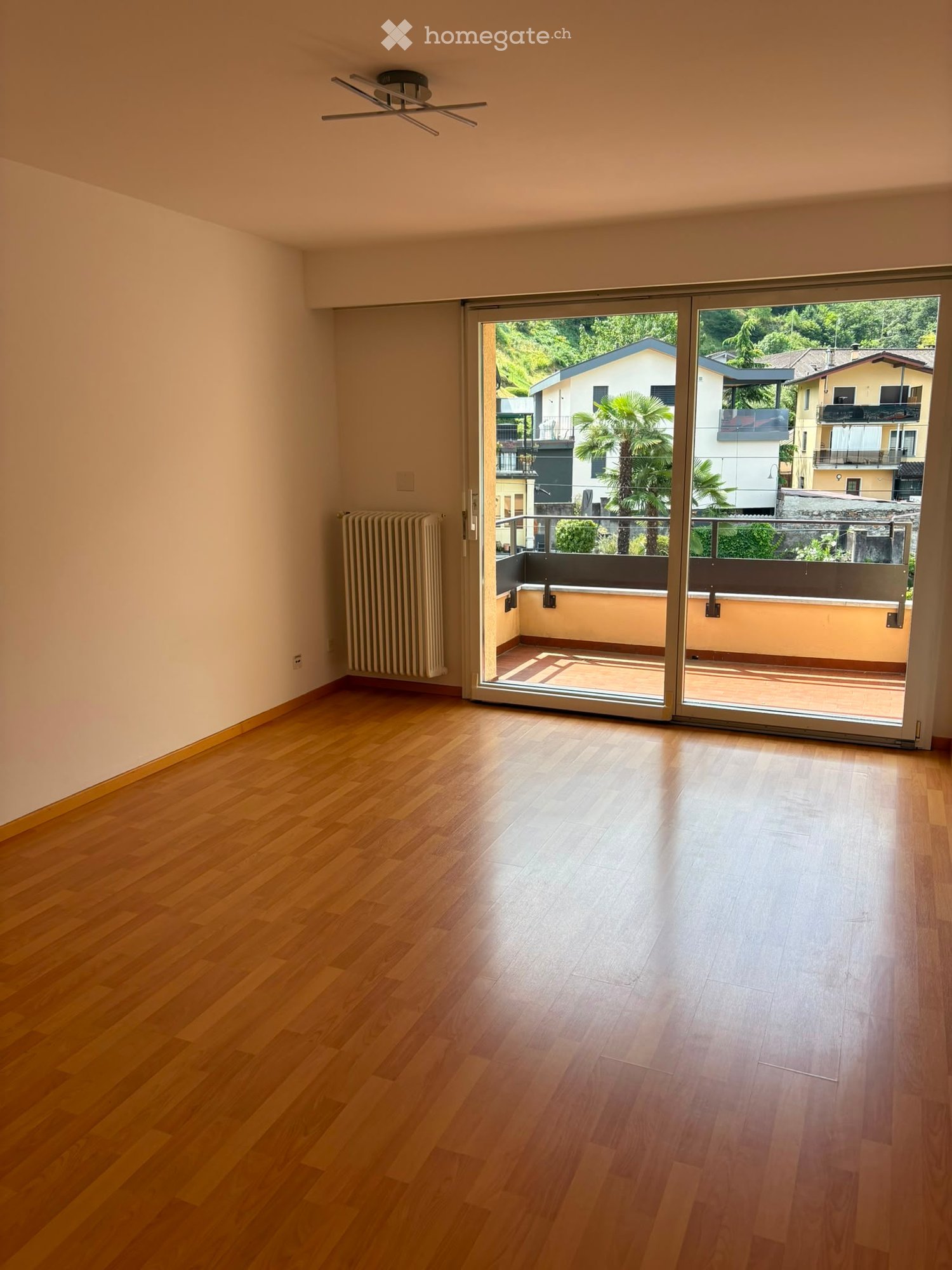 Empty room with wooden flooring, large sliding glass doors leading to a balcony with a view of the surrounding area.
