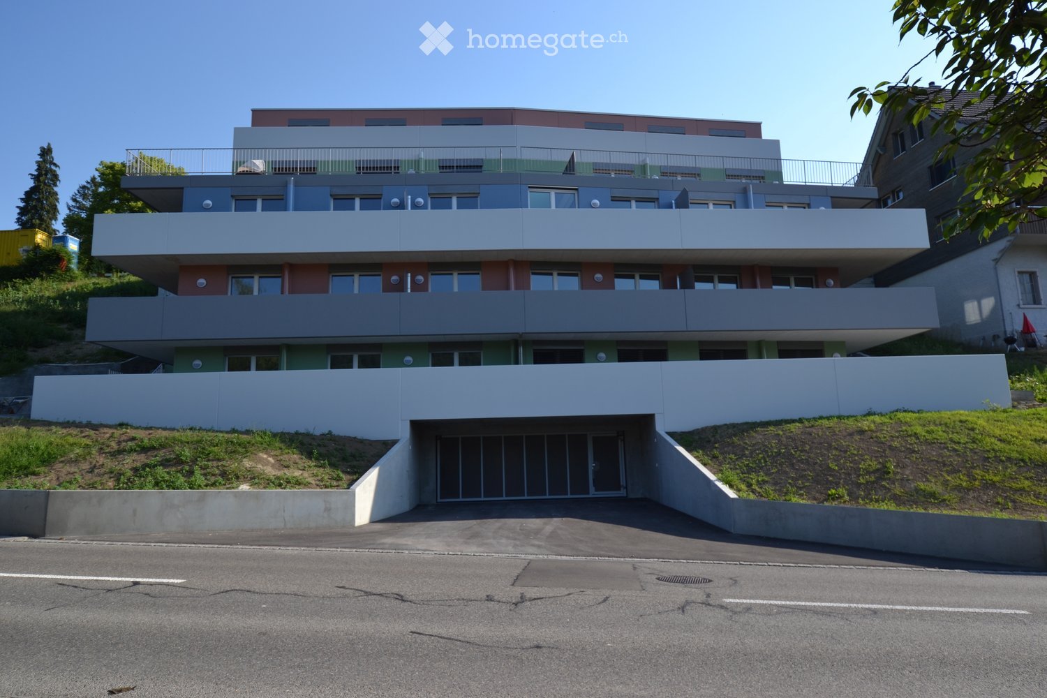 Modern multi-story residential building with balconies, white and green facade, and a raised ground floor entrance.