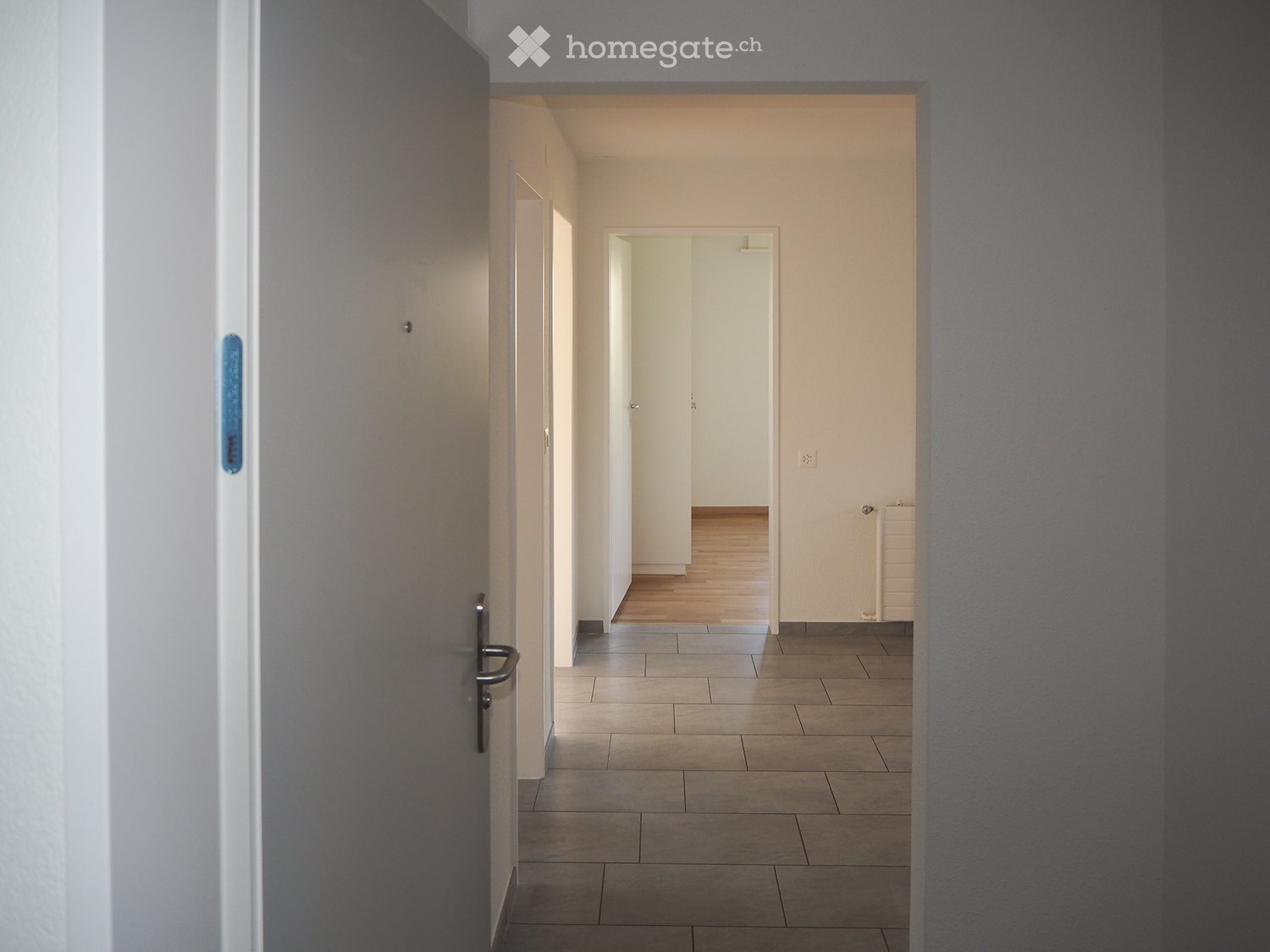 Empty hallway with tiled floor, white walls, and multiple doors leading to other rooms.
