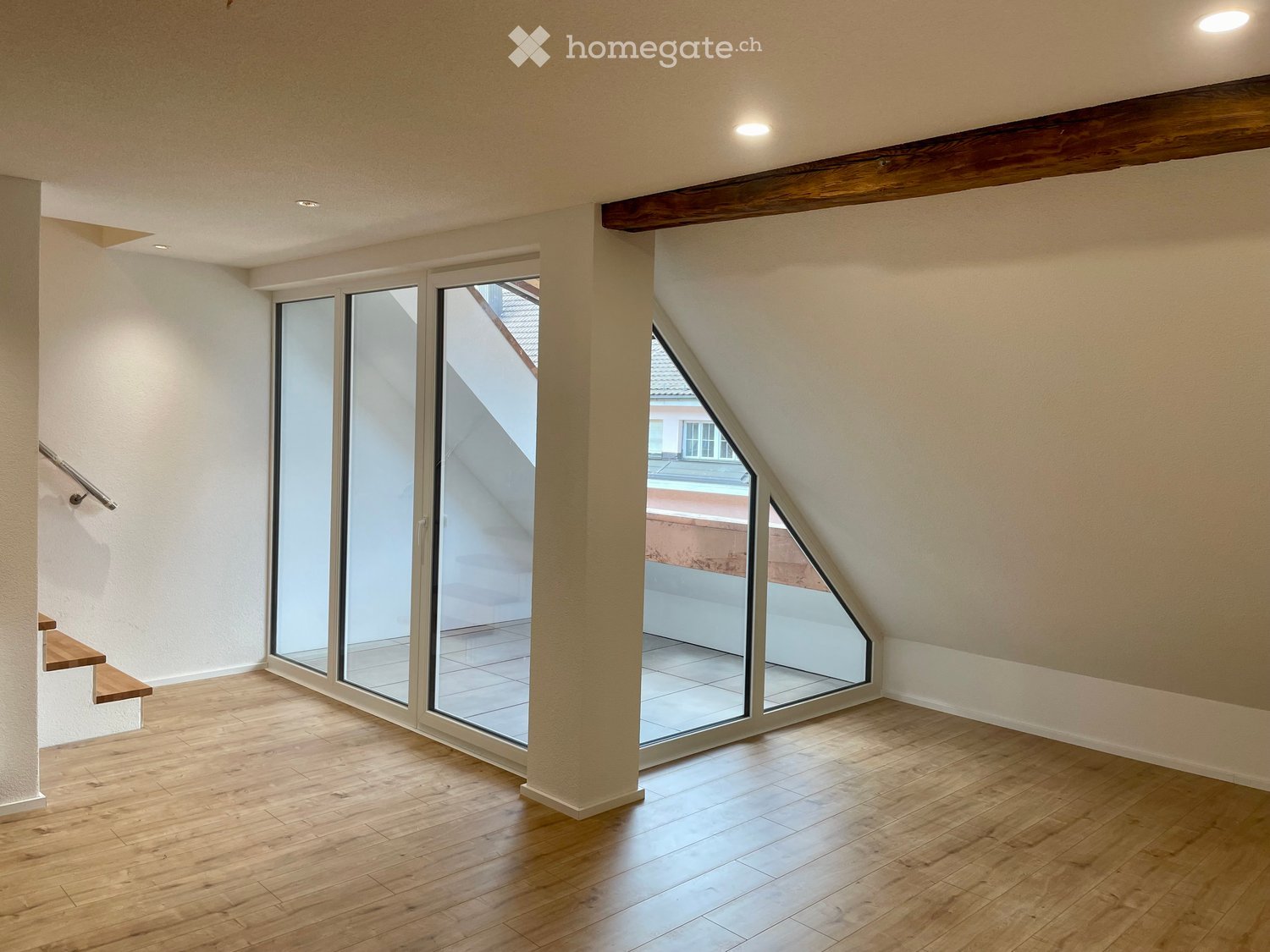 Empty attic room with wooden flooring, large skylight windows, and exposed wooden beams on the ceiling.