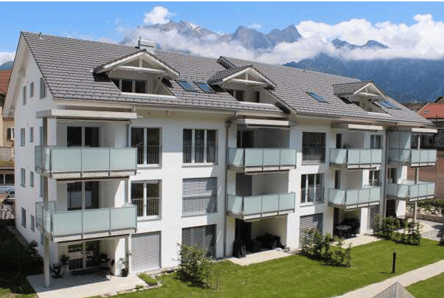 Modern multi-story residential building with multiple balconies and a scenic mountain view in the background.