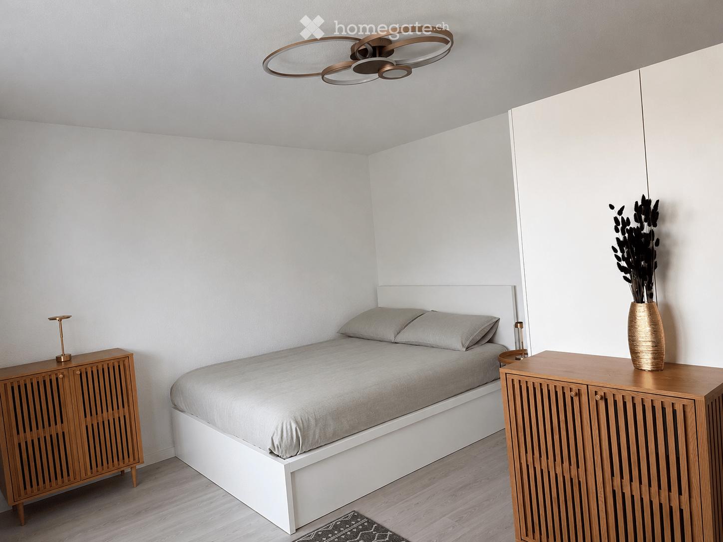 Modern bedroom with a white bed, grey bedding, wooden nightstands, and a decorative vase on one nightstand.