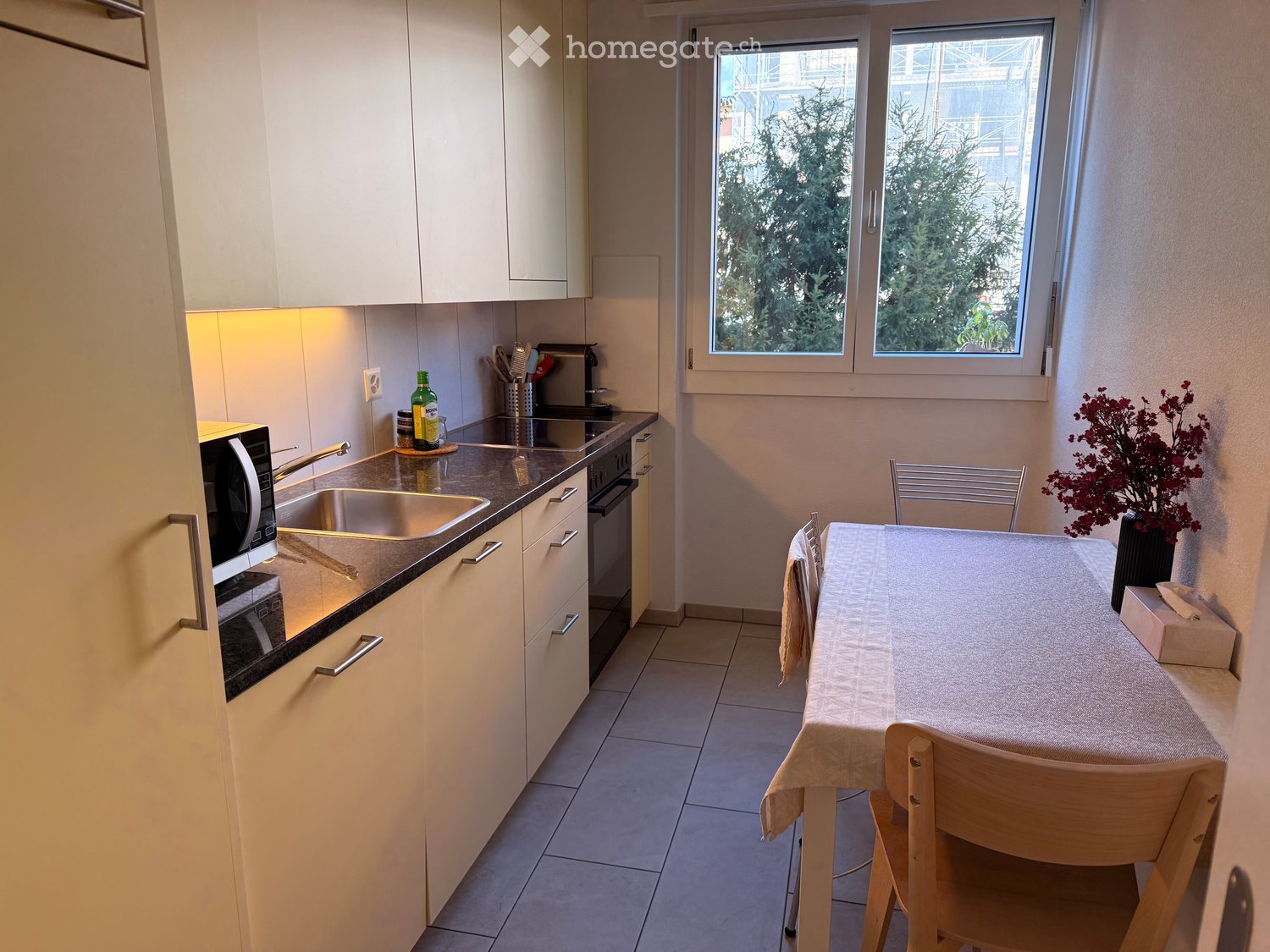 Modern kitchen with white cabinets, stainless steel sink, microwave, and a small dining area with a table and chairs.