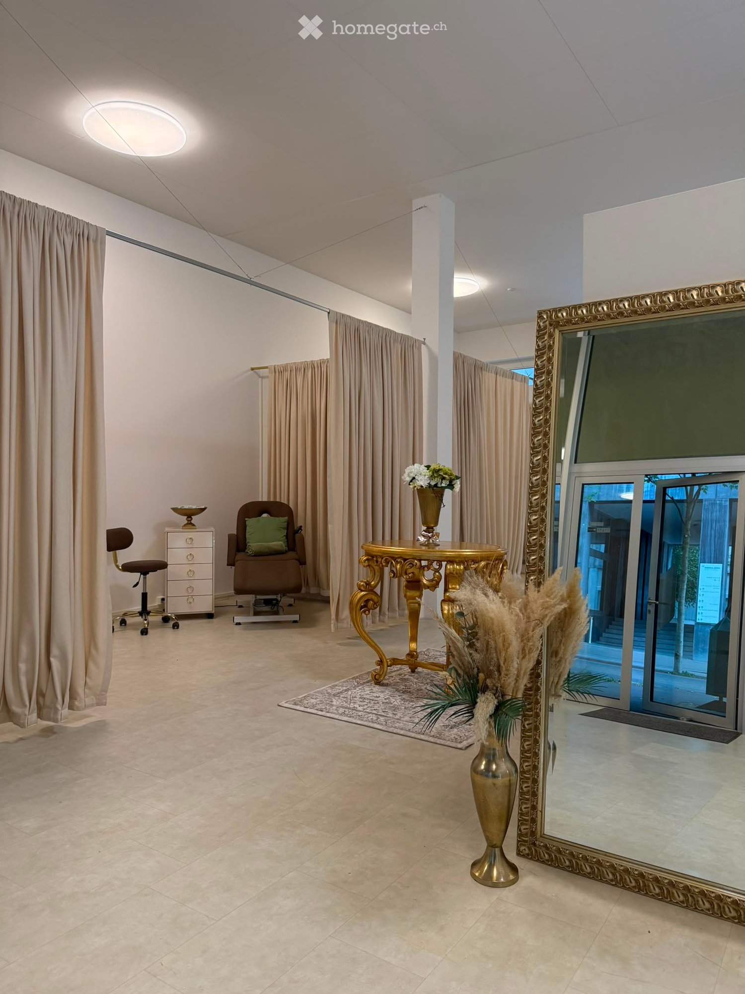 Elegant room with beige curtains, a large ornate mirror, a golden table with vase, and decorative plants.