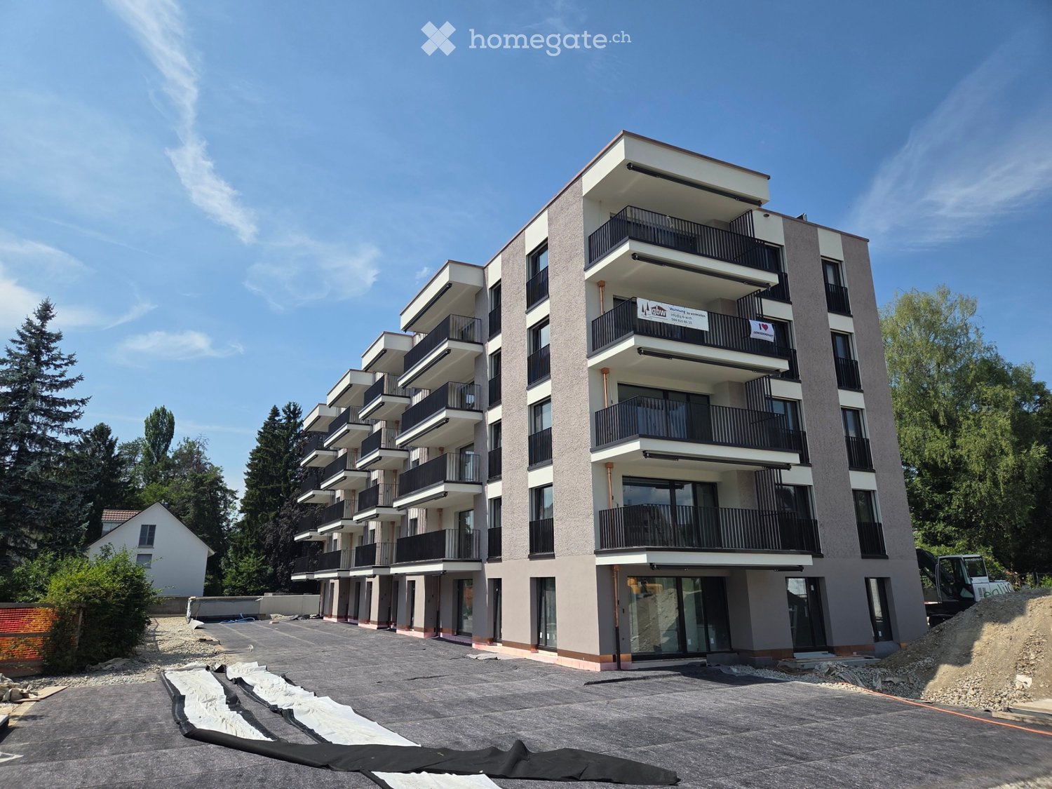 Modern multi-story apartment building with balconies, surrounded by trees and under construction.