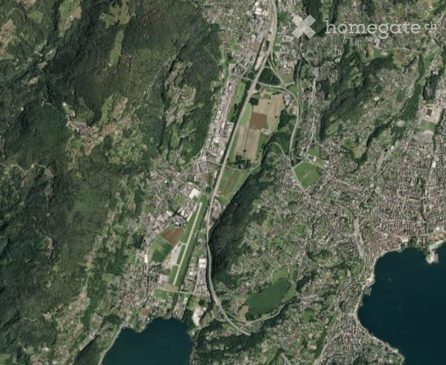 Aerial view of a cityscape with residential and commercial buildings, roads, green spaces, and water bodies.
