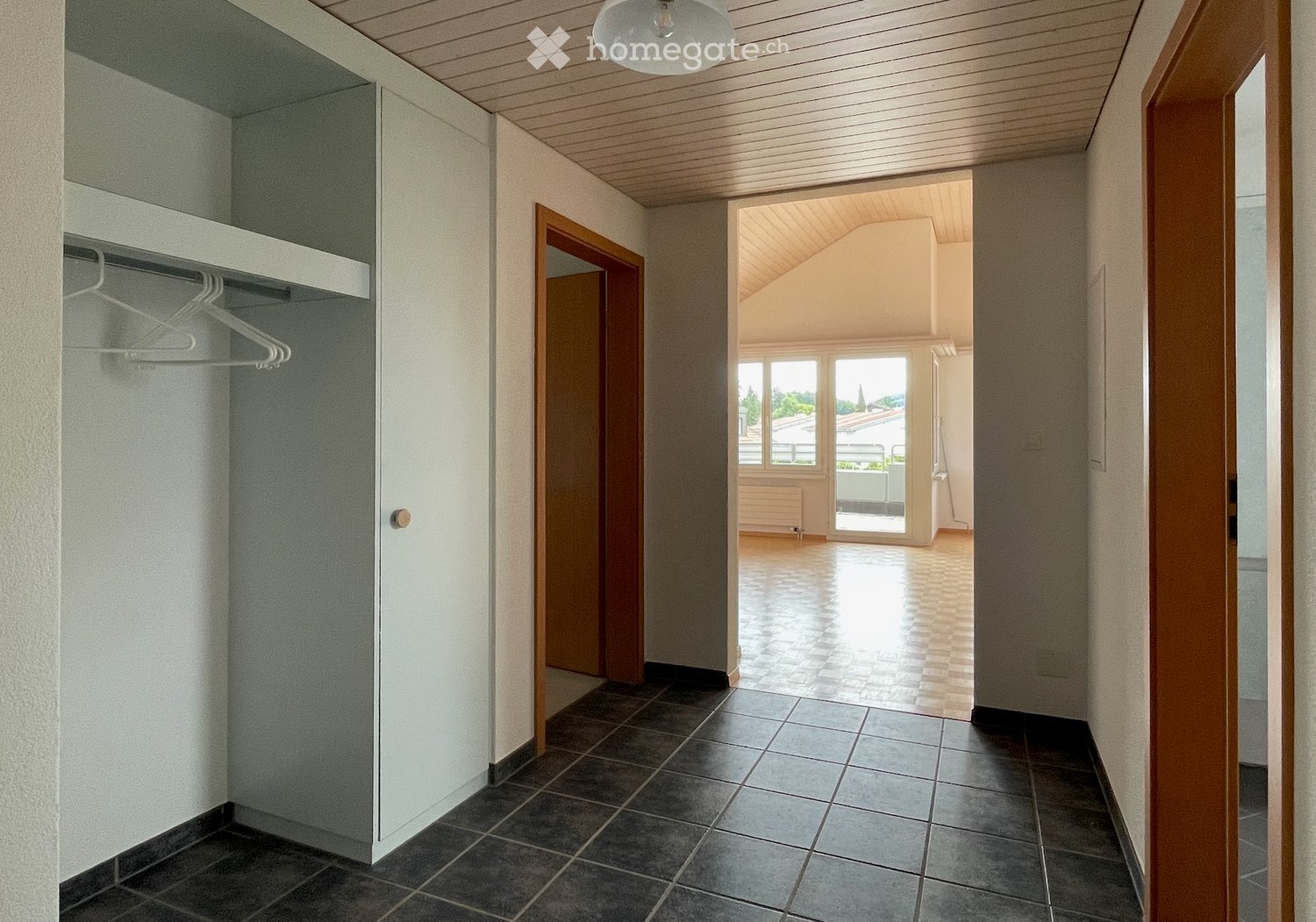A modern hallway with tiled flooring, white walls, and wooden doors leading to other rooms. Features a built-in closet with hanging space and a ceiling light fixture.