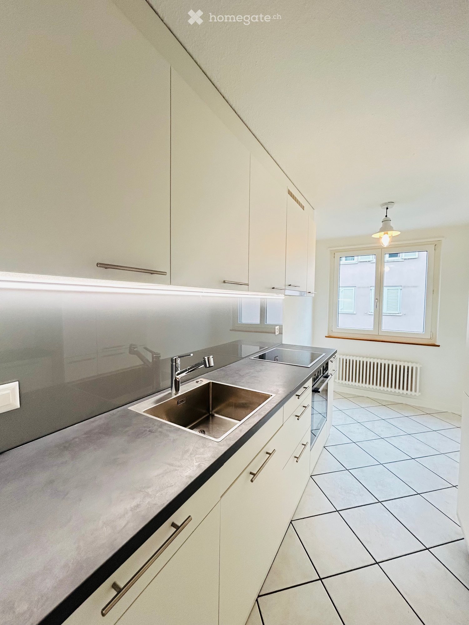 Modern kitchen with white cabinets, stainless steel sink, tiled floor, and large windows.