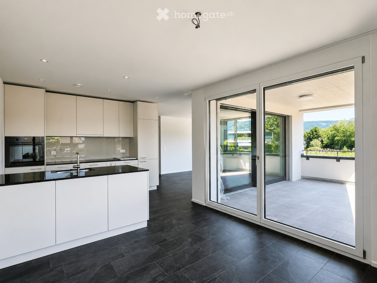 Modern kitchen with white cabinets, black countertops, and large glass sliding doors leading to a balcony with scenic views.