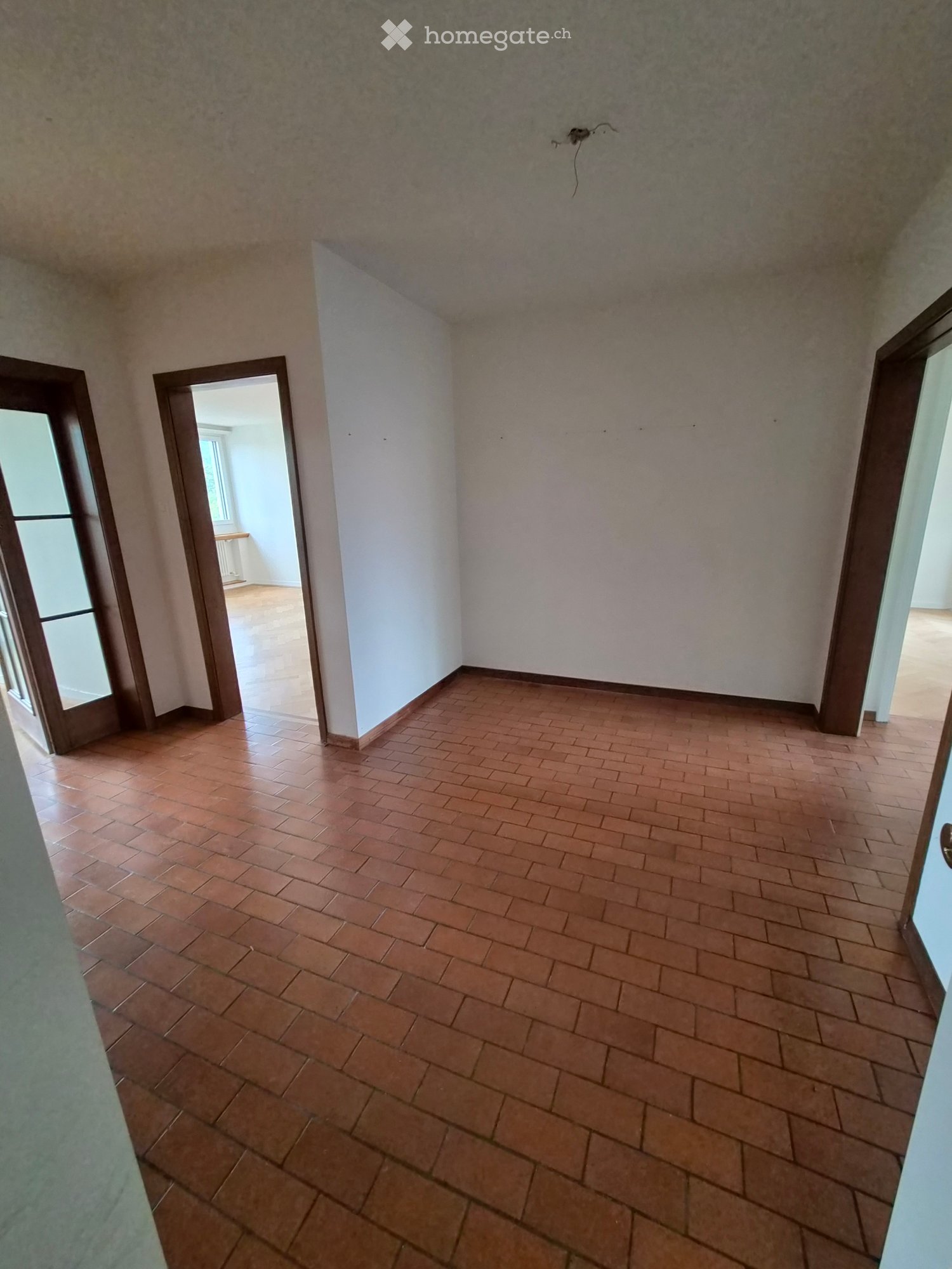 Empty room with tiled floor and white walls, featuring an open doorway leading to another room.