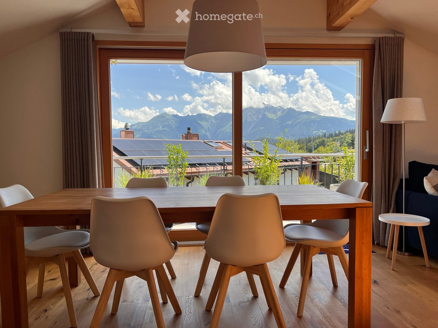 Bright dining area with wooden table, modern chairs, pendant lamp, and large windows offering mountain views.