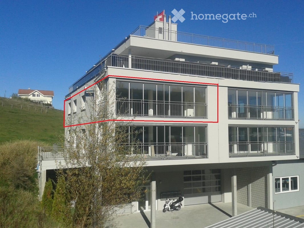 Modern multi-story building with large glass windows and balconies, situated on a hillside with a clear view.