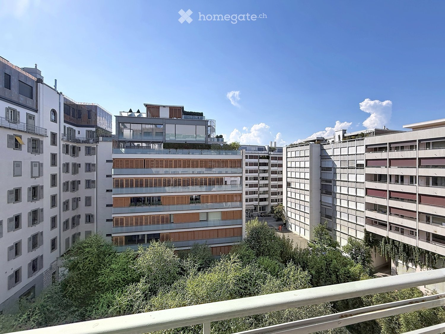 View of a multi-story residential building complex with balconies, windows, and greenery in the foreground.