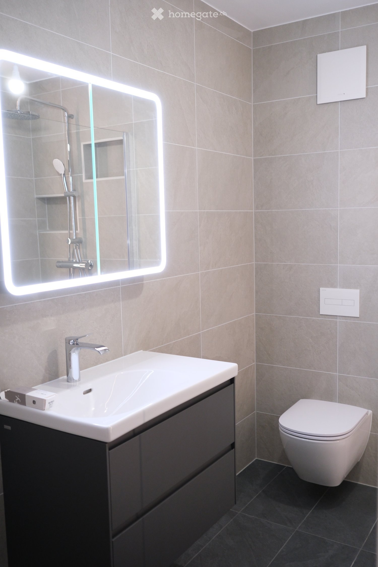 Modern bathroom with a white sink, sleek faucet, illuminated mirror, toilet, and dark cabinet.