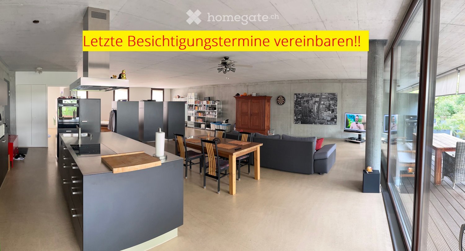 Open-plan living and dining area with a grey sofa, wooden dining table, kitchen island, and modern appliances.