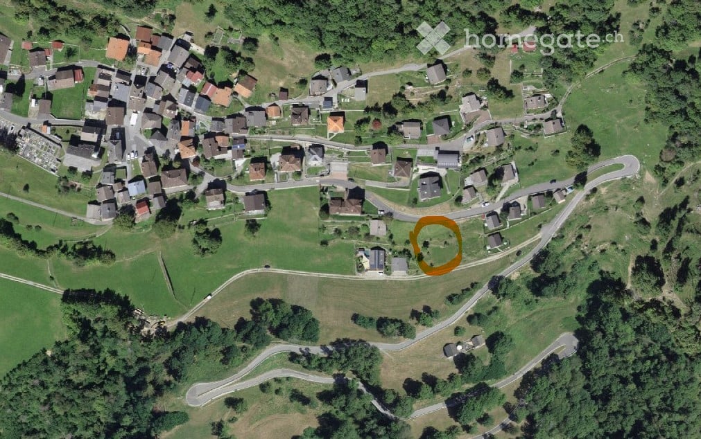 Aerial view of a rural village with scattered houses, roads, and green fields.
