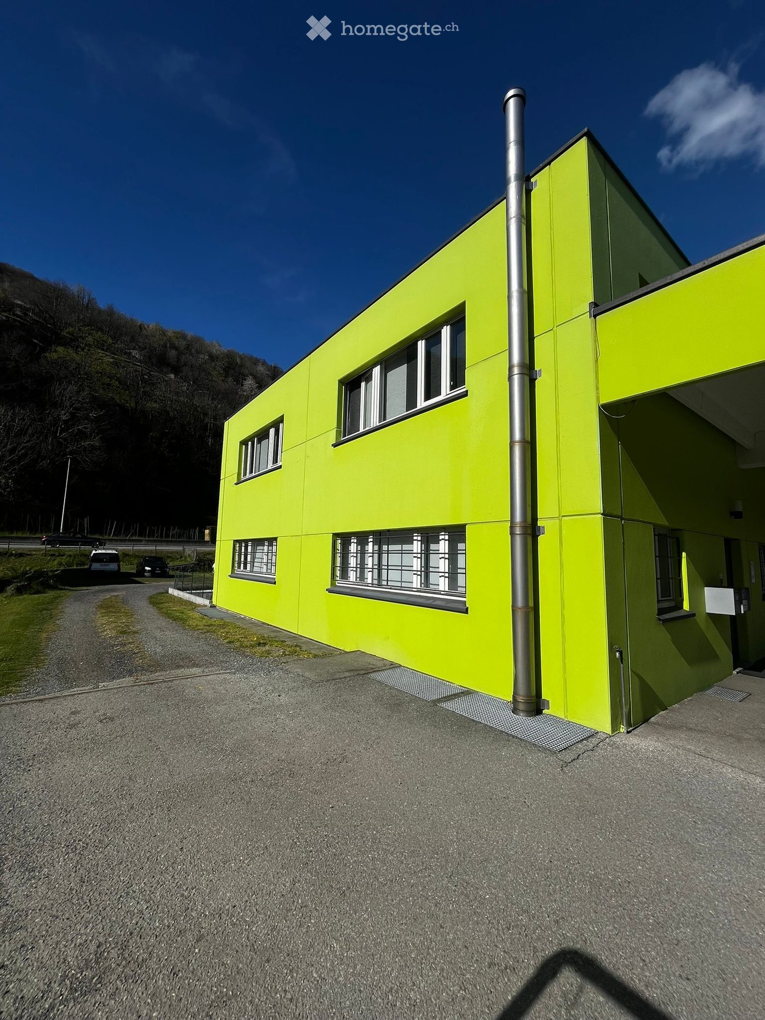 2 story building, yellow exterior, multiple windows, metal pipe, paved road, grassy area