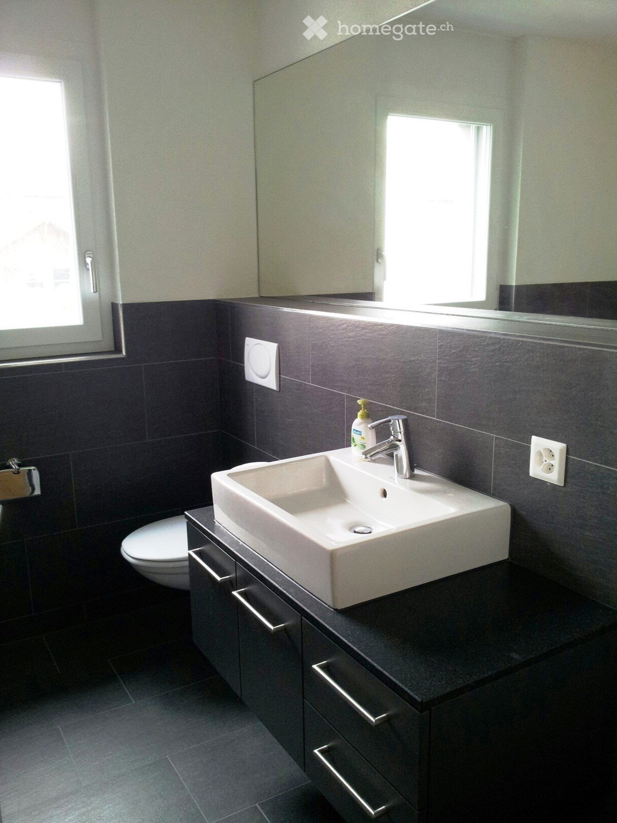 Modern bathroom with a white sink, chrome faucet, dark grey tiles, and a built-in cabinet.