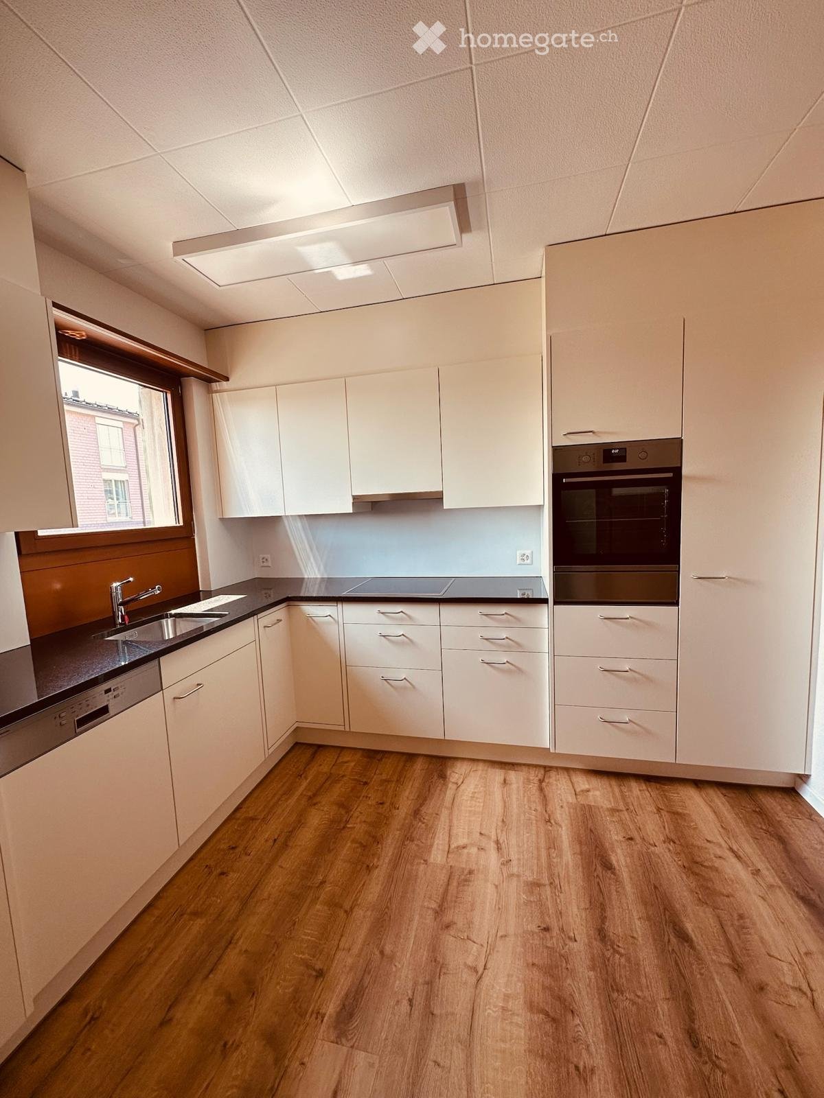 Modern kitchen with white cabinets, wooden flooring, and stainless steel appliances including a sink, oven, and dishwasher.