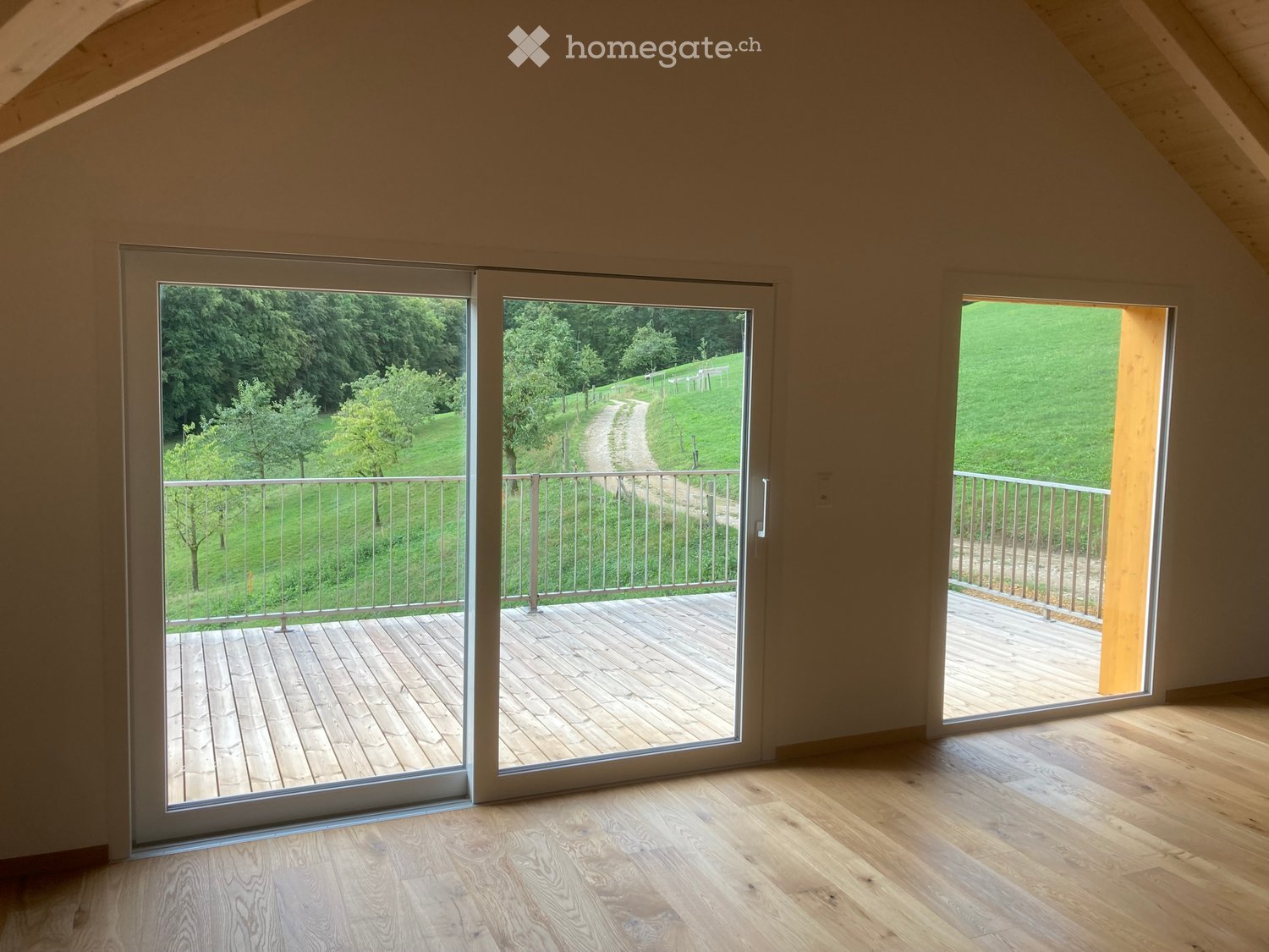 Bright, empty room with wooden flooring and large sliding glass doors leading to a wooden deck and outdoor area.