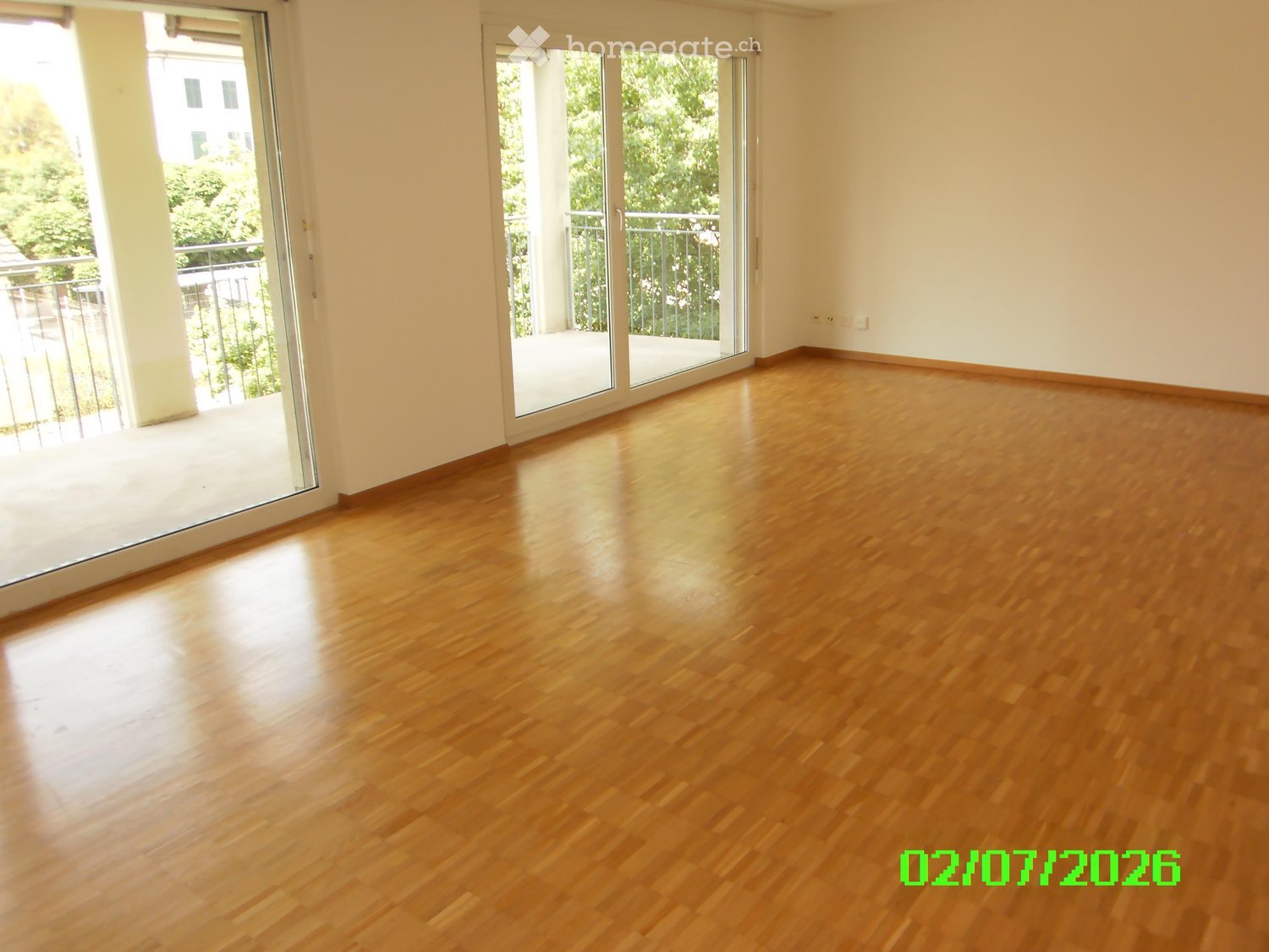 Empty room with wooden flooring and large sliding glass doors leading to a balcony.