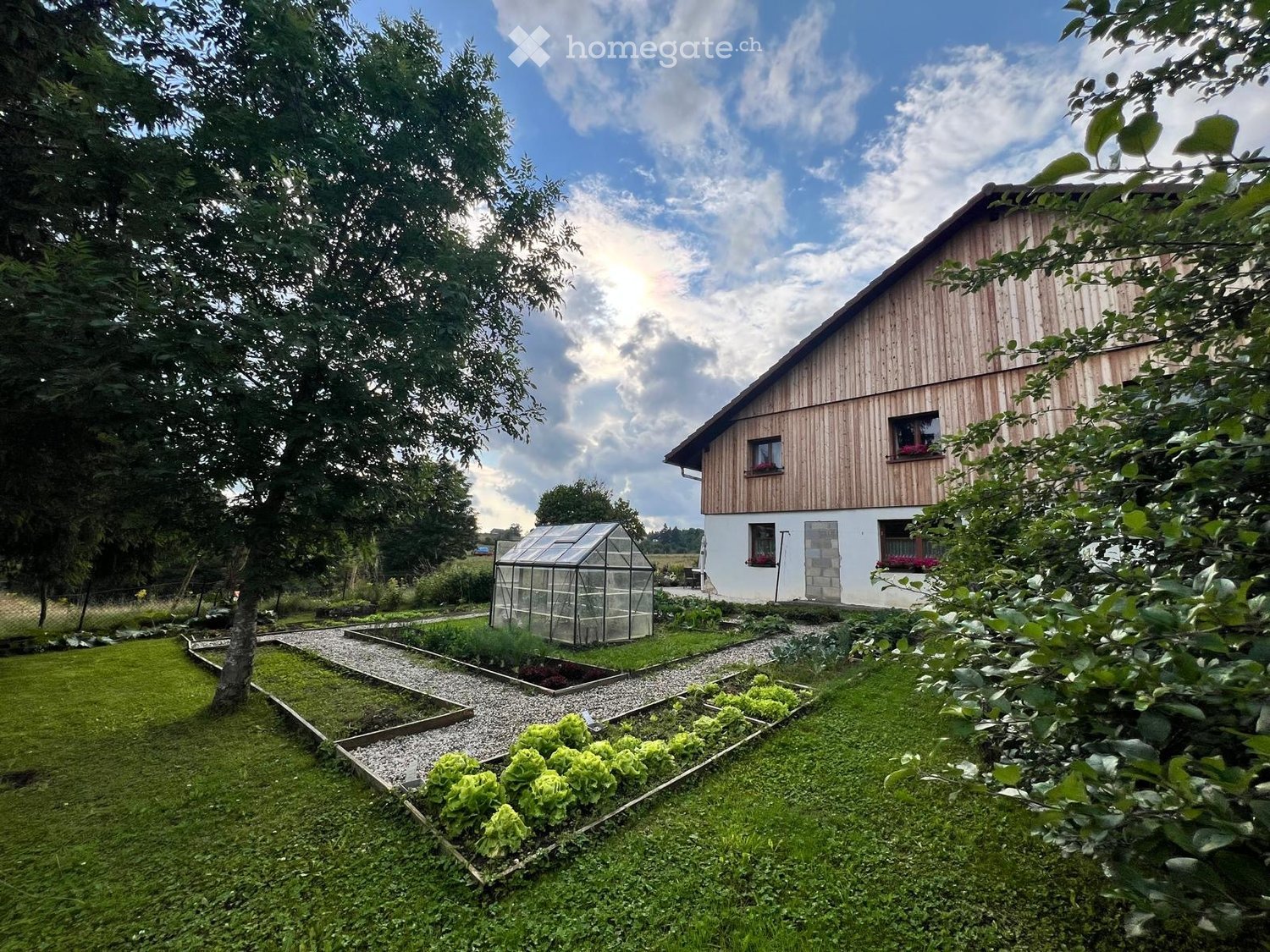 A well-maintained garden with a wooden house, raised garden beds, a greenhouse, and lush greenery.