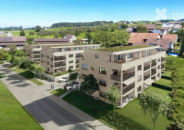 A modern multi-story residential building with balconies and large windows, surrounded by green lawns and trees.