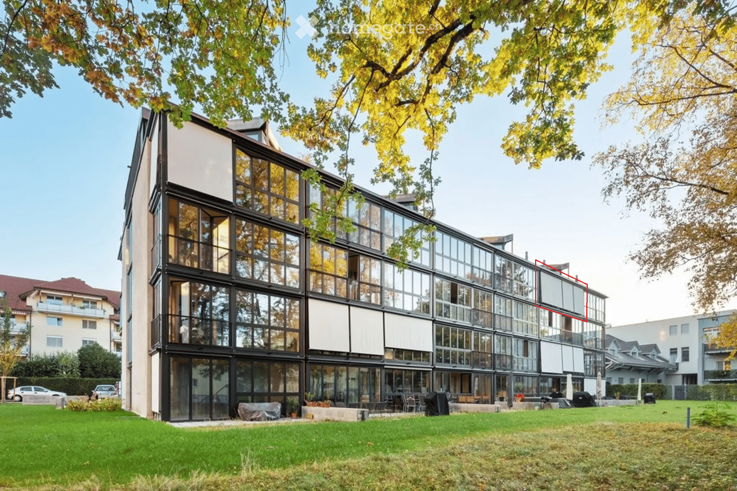 Modern multi-story building with large glass windows and a sleek design, surrounded by a well-maintained lawn and trees.