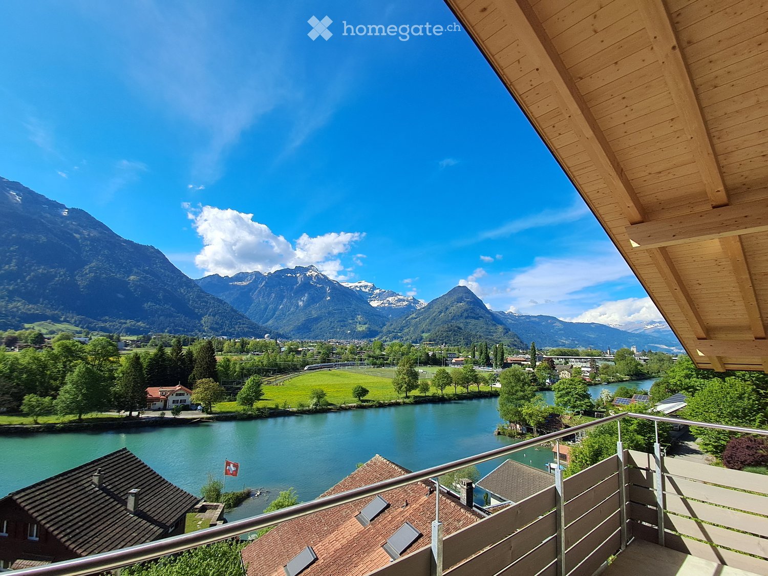 Balcony overlooking a scenic valley with a river, distant mountains, and a small town.