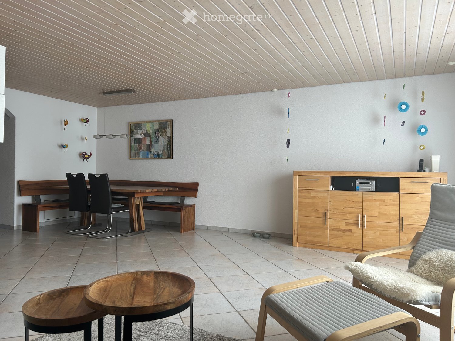 Modern living room with wooden furniture, including a dining table with chairs, a bench, a cabinet, and a small round table with two chairs.
