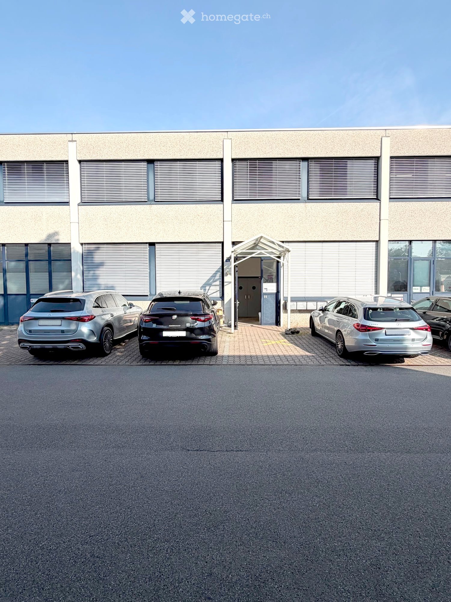 Modern building with large windows and a covered entrance, with several cars parked in front.