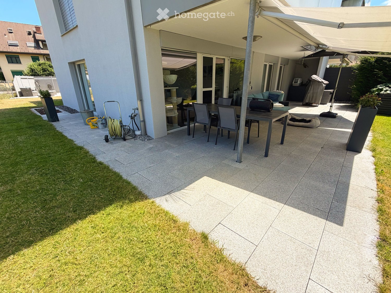 Patio area with a dining table, chairs, umbrella, and a well-maintained lawn.