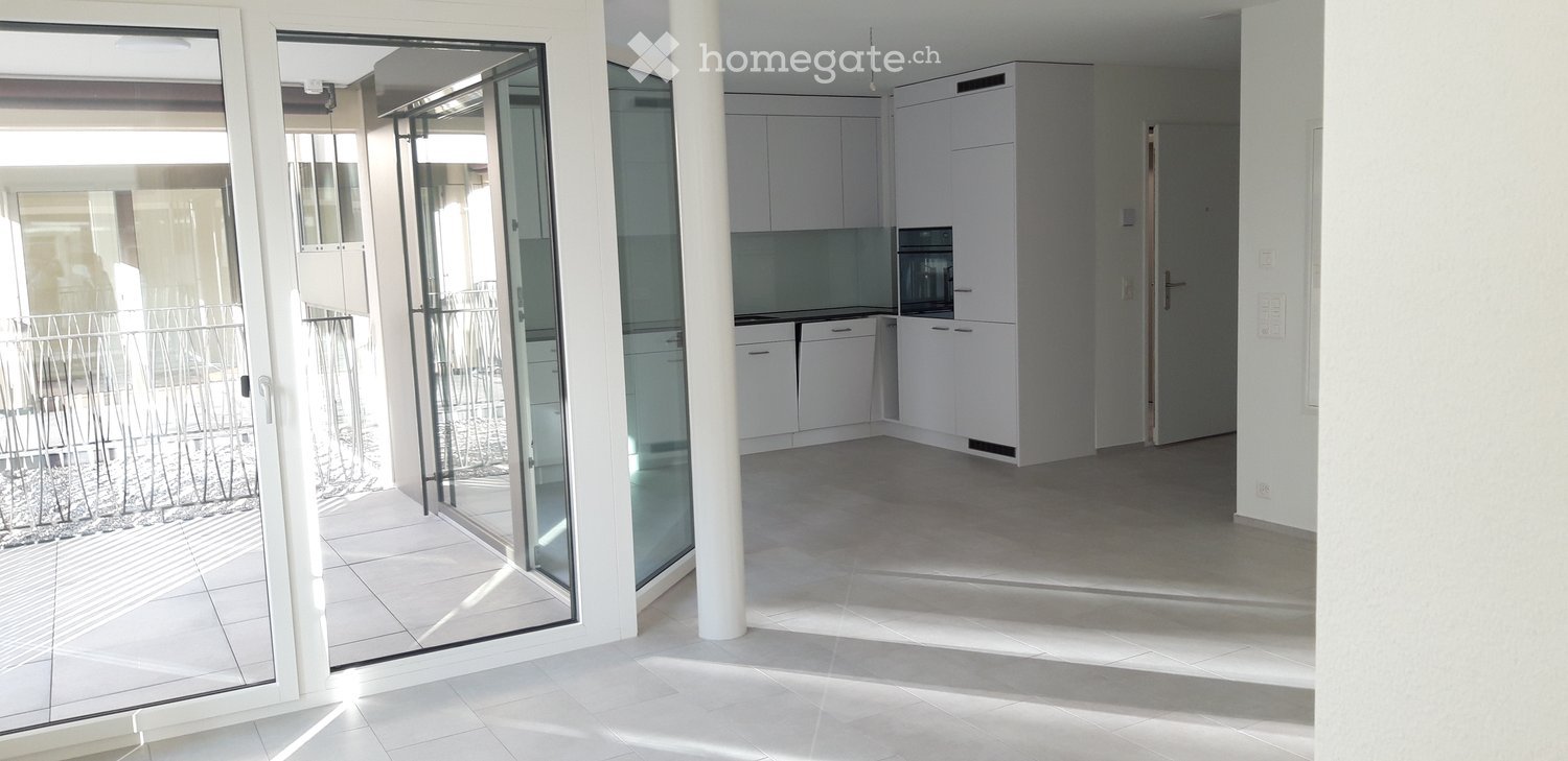 Empty kitchen with white cabinets, a microwave, and a tiled floor, connected to a balcony through large glass doors.