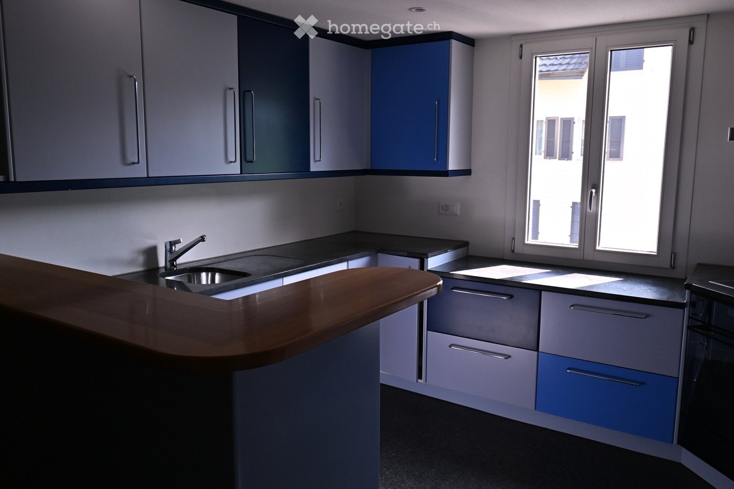 Modern kitchen with grey and blue cabinets, a wooden countertop, and a stainless steel sink.