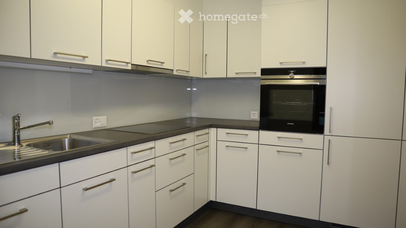 Modern kitchen with white cabinets, stainless steel sink, faucet, and built-in oven.