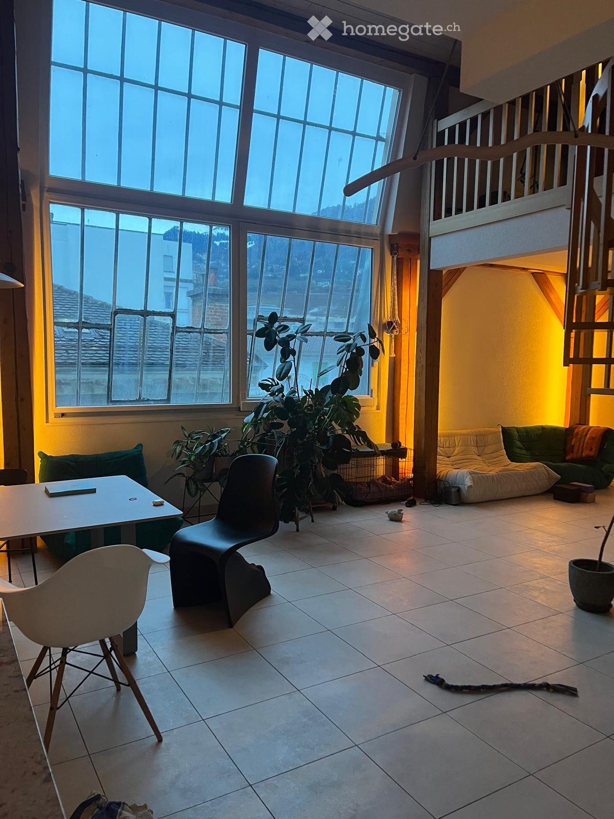 Bright living room with large windows, tiled floor, modern furniture including a sofa, chairs, and a table, with plants and a cozy seating area.