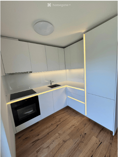 Modern, minimalist kitchen with white cabinets, wooden flooring, and built-in appliances including an oven and sink.